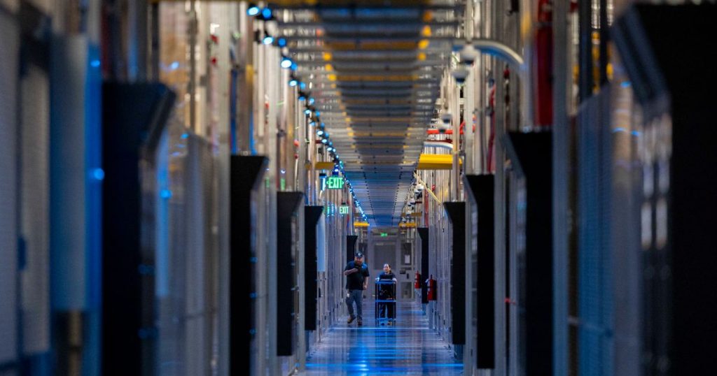 Pasillo de un centro de datos con racks de servidores iluminados en azul y dos técnicos trabajando, infraestructura similar a la usada por VAST Data